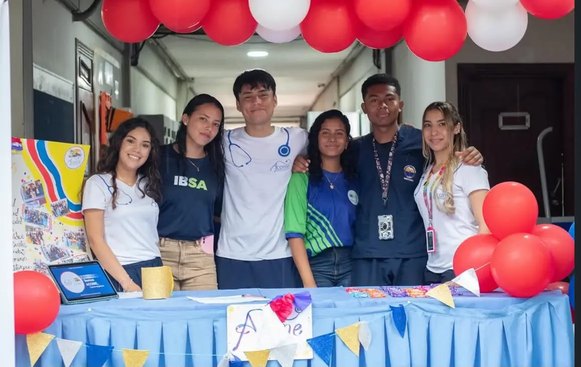 Estudiantes posan en un stand decorado con globos rojos y blancos.