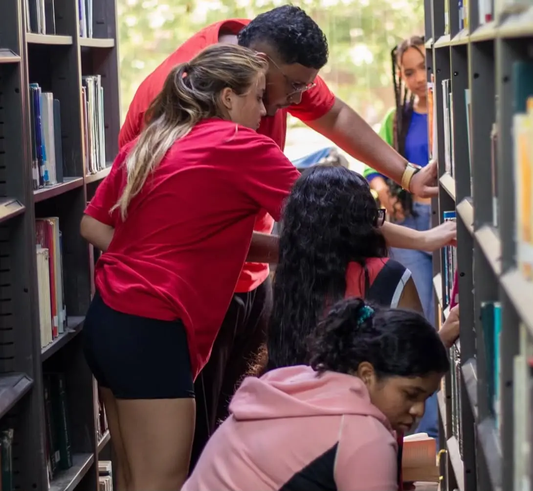 Estudiantes buscan entre los estantes de la biblioteca durante una dinámica.